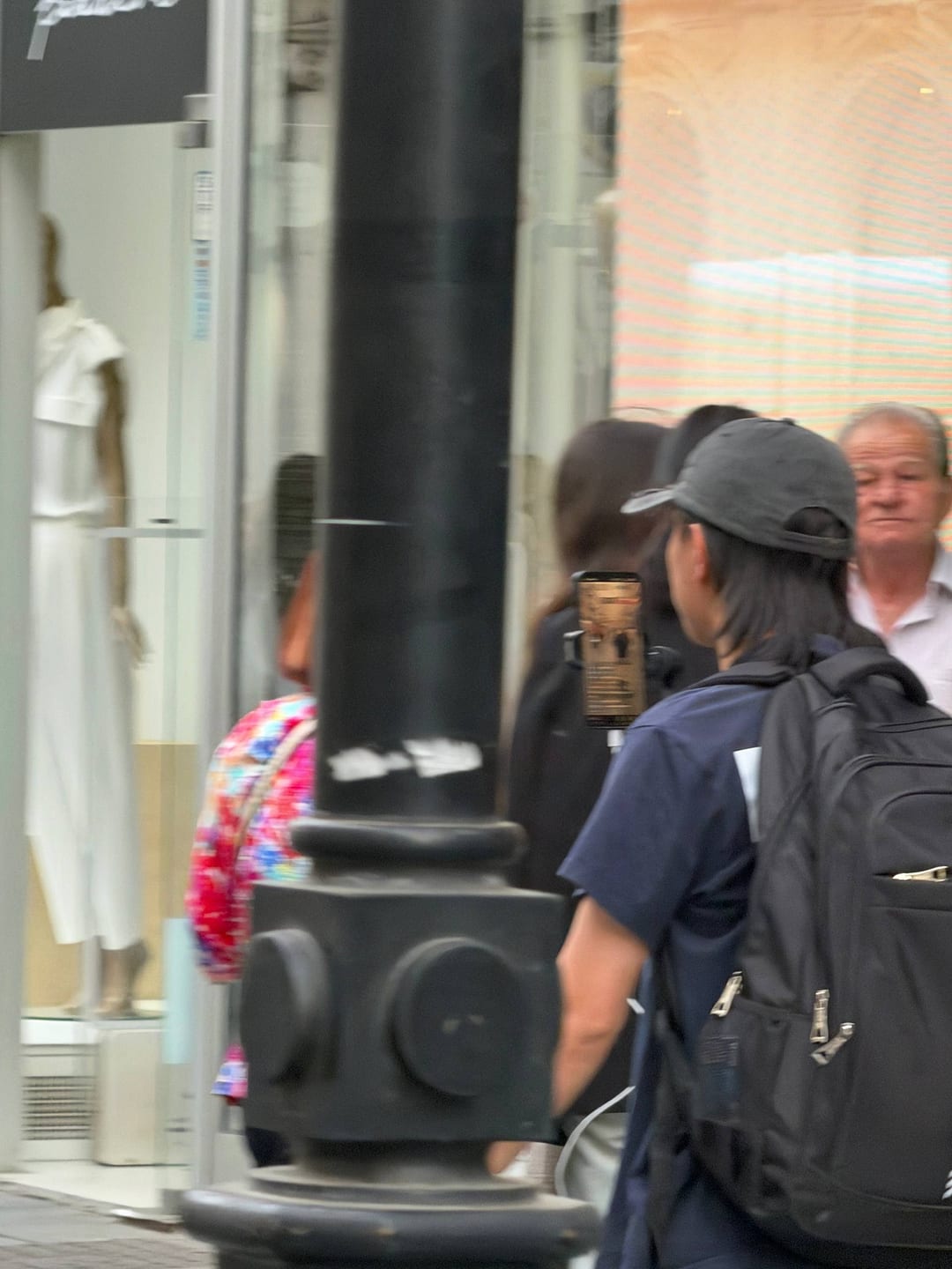 A blurred street scene: a person holding a phone on a stick, pointed toward a crowd of pedestrians.