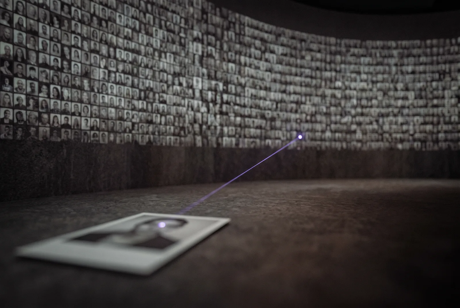 A vast dark wall of thousands of tiny blurred portrait thumbnails. From a single photo card in the foreground a thin violet line travels across the wall and lands on one distant thumbnail.